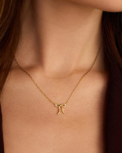 Gold necklace with a bow pendant on a person's neck