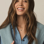 Woman wearing a light blue vest over a blue shirt with a neutral background