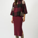 Woman wearing a burgundy and black checkered top with a matching skirt on a white background