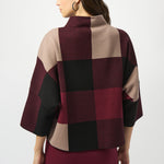 Woman wearing a checkered poncho with maroon, beige, and black pattern on a white background