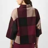 Woman wearing a checkered poncho with maroon, beige, and black pattern on a white background