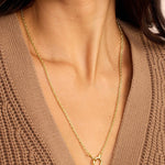 Gold necklace worn by a person in a brown sweater