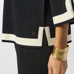 Black outfit with white trim and gold cuff on a plain background
