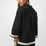Woman wearing a black outfit with white trim on a plain background
