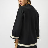Woman wearing a black outfit with white trim on a plain background
