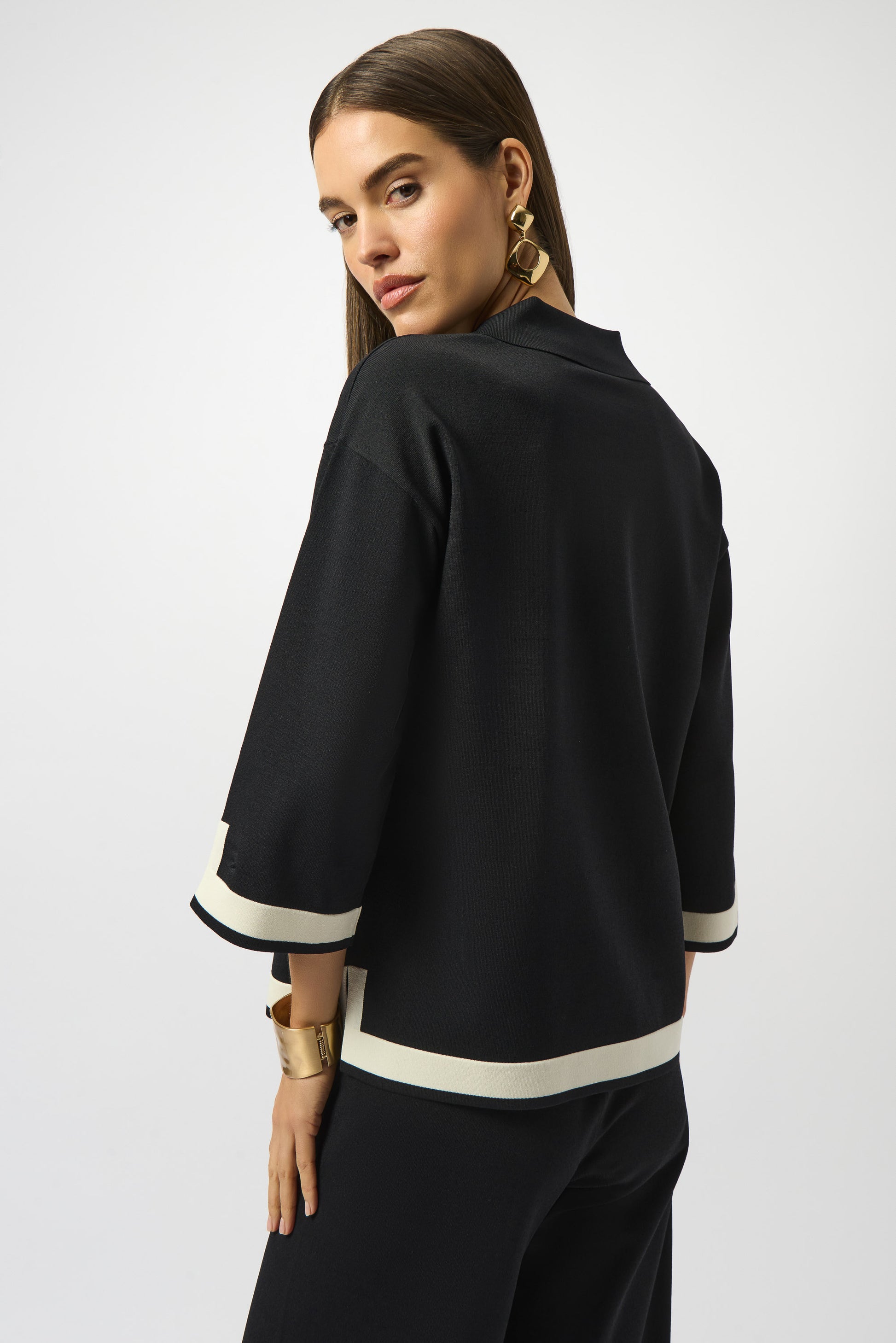 Woman wearing a black outfit with white trim on a plain background