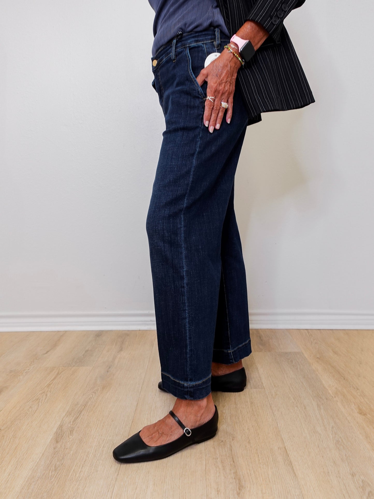 Person wearing dark blue jeans and a black outfit against a white wall.