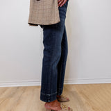 Person wearing a plaid blazer, dark jeans, and beige shoes on a light wooden floor.