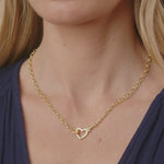 Gold necklace with a heart pendant worn by a person against a neutral background