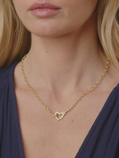 Gold necklace with a heart pendant worn by a person against a neutral background