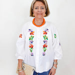 Woman wearing a white blouse with colorful floral embroidery on a plain background