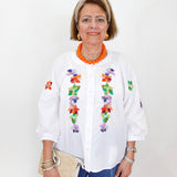 Woman wearing a white blouse with colorful floral embroidery on a plain background