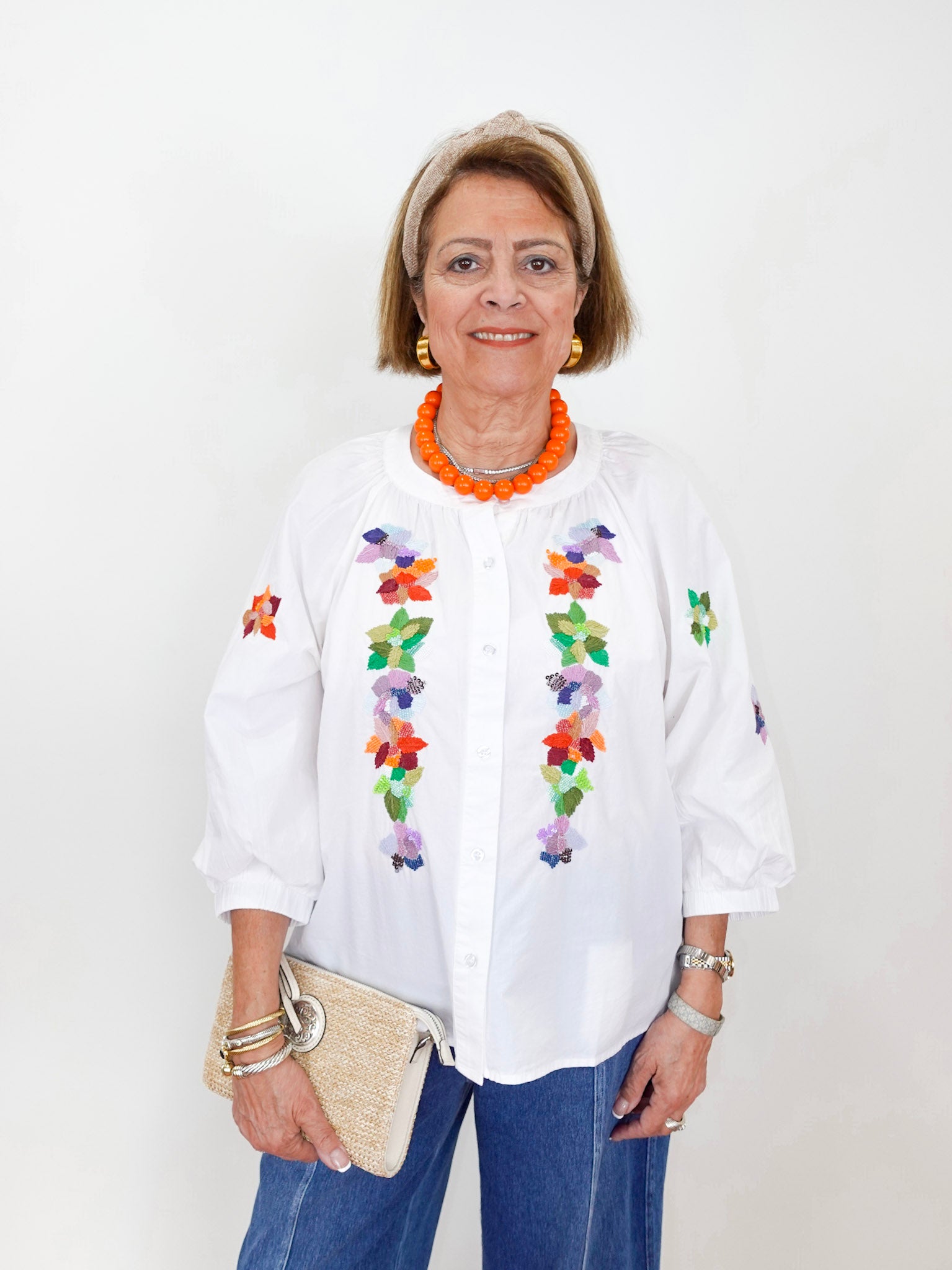 Woman wearing a white blouse with colorful floral embroidery on a plain background