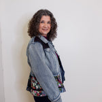 Woman wearing a denim jacket over a floral top against a white wall