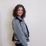 Woman wearing a denim jacket over a floral top against a white wall