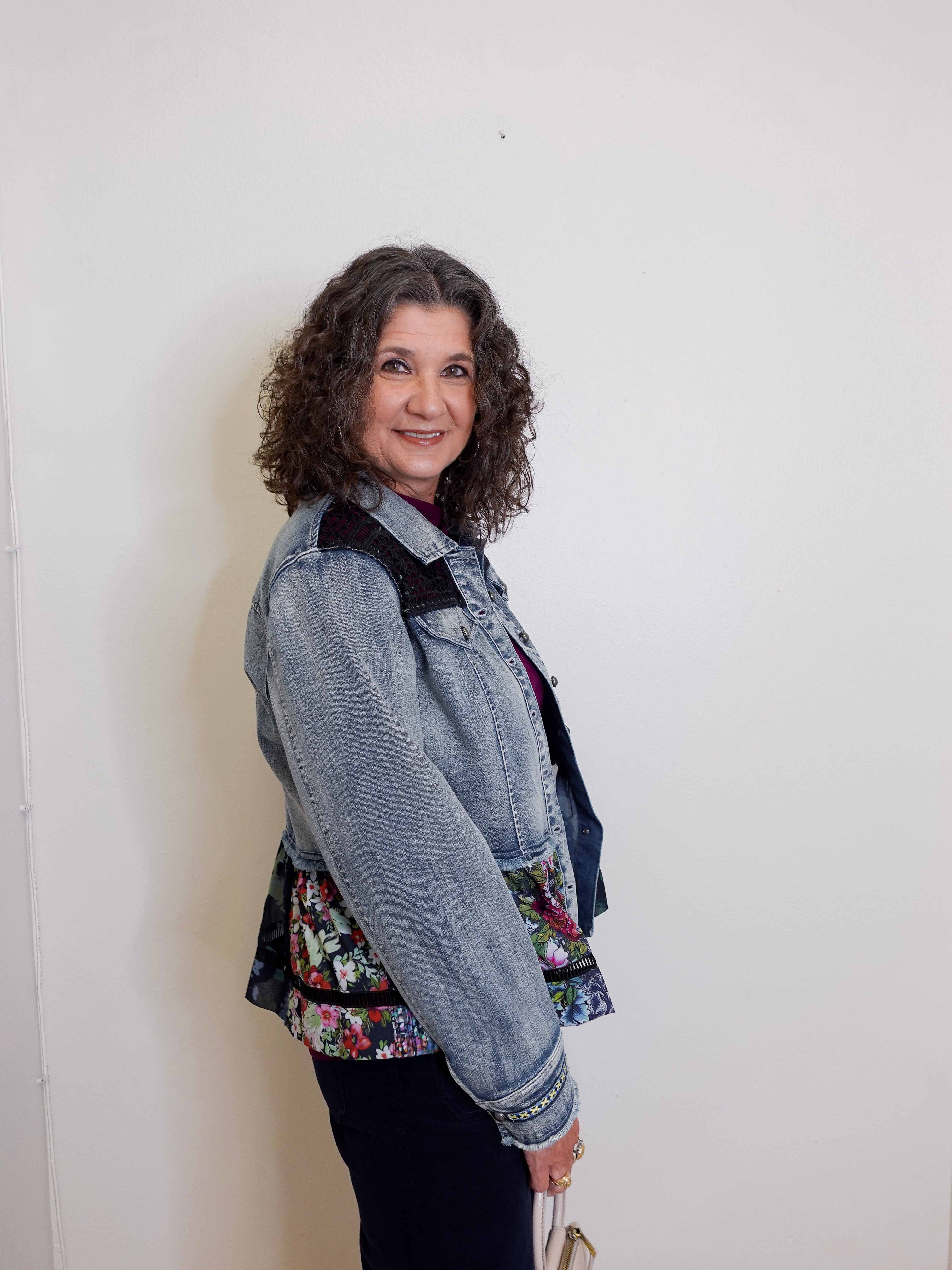 Woman wearing a denim jacket over a floral top against a white wall