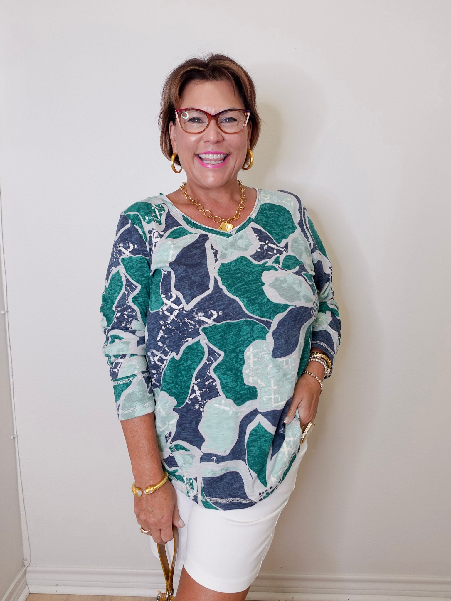 Woman wearing a patterned top and white pants against a plain background