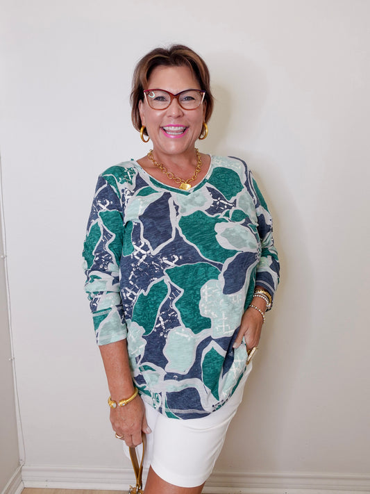 Woman wearing a patterned top and white pants against a plain background