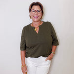 Woman wearing an olive green shirt and white shorts against a plain background