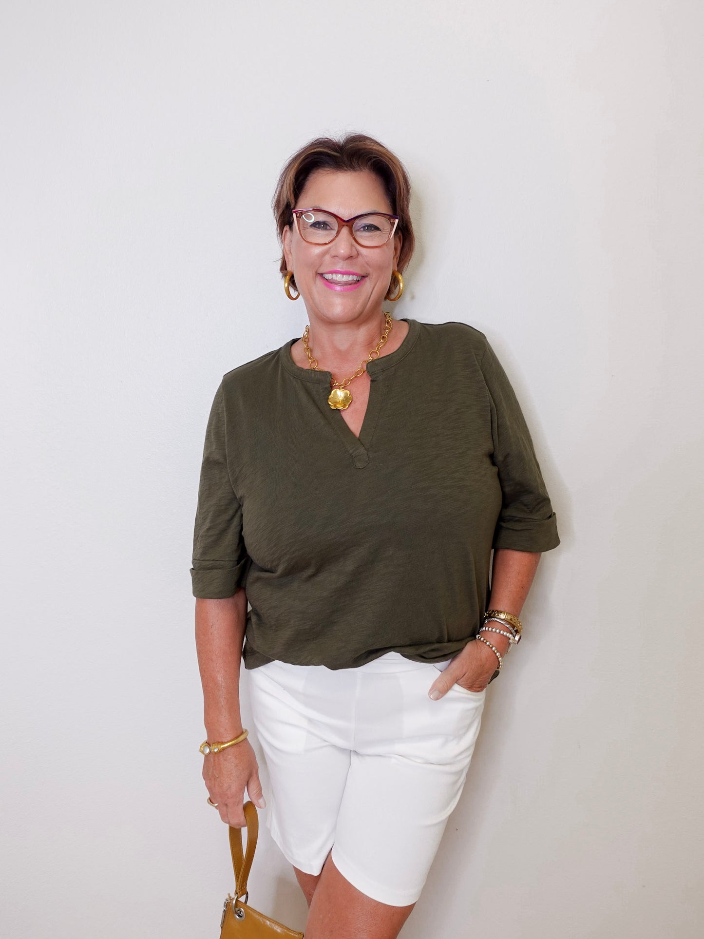 Woman wearing an olive green shirt and white shorts against a plain background