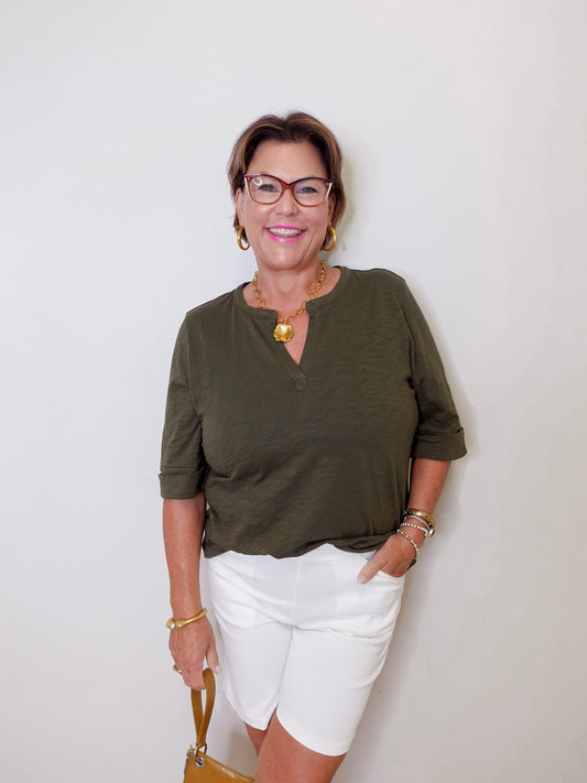 Woman wearing an olive green shirt and white shorts against a plain background
