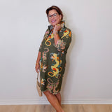 Woman wearing a patterned dress standing against a plain white wall.