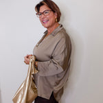 Woman wearing glasses and a beige shirt, holding a gold bag against a white wall.