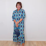 Woman wearing a blue patterned dress standing against a white wall.