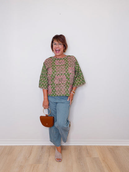 Woman wearing a patterned top and jeans, holding a handbag against a white wall.