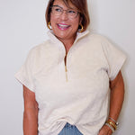 Woman wearing a cream-colored zip-up sweater and blue jeans against a white background