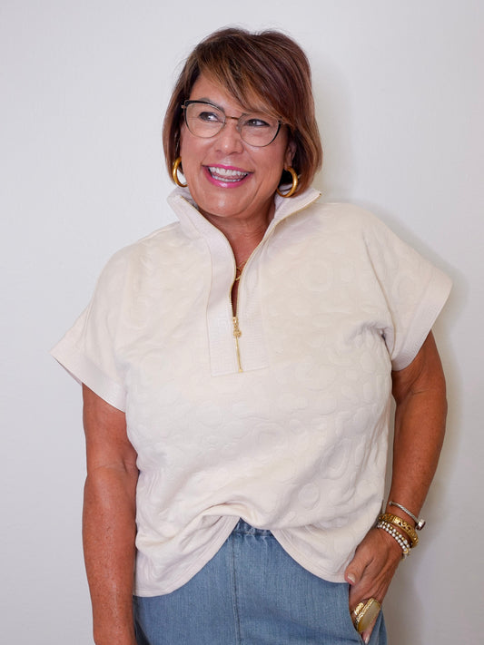 Woman wearing a cream-colored zip-up sweater and blue jeans against a white background