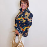 Woman wearing a colorful dragon patterned jacket holding a gold handbag against a white wall.