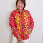 Woman wearing a pink floral blouse with a beige handbag against a white background