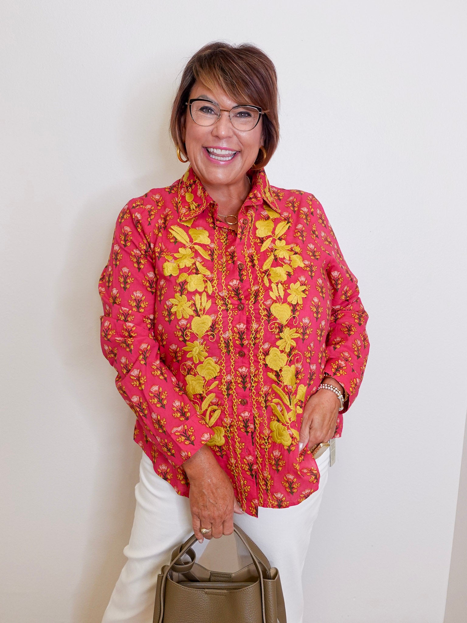 Woman wearing a pink floral blouse with a beige handbag against a white background