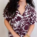 Woman wearing a maroon and white patterned blouse against a plain background