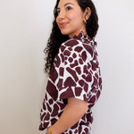 Woman wearing a maroon and white patterned blouse against a plain background