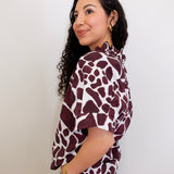 Woman wearing a maroon and white patterned blouse against a plain background