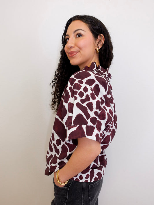 Woman wearing a maroon and white patterned blouse against a plain background