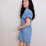 Woman wearing a blue dress against a white wall
