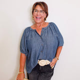 Woman wearing a blue blouse and dark pants against a white background