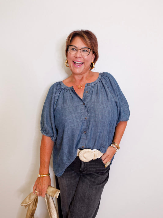 Woman wearing a blue blouse and dark pants against a white background