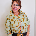 Woman wearing a light green jacket with gold tiger patterns against a plain background