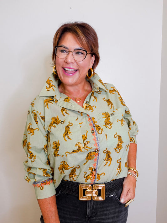 Woman wearing a light green jacket with gold tiger patterns against a plain background