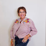 Woman wearing a patterned blouse with floral embroidery against a plain background