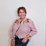 Woman wearing a patterned blouse with floral embroidery against a plain background