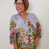 Woman wearing a colorful floral blouse with leopard print sleeves against a white background