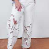 Person wearing white lace pants with a plain background