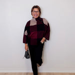 Person wearing a patterned sweater and black pants against a white wall.