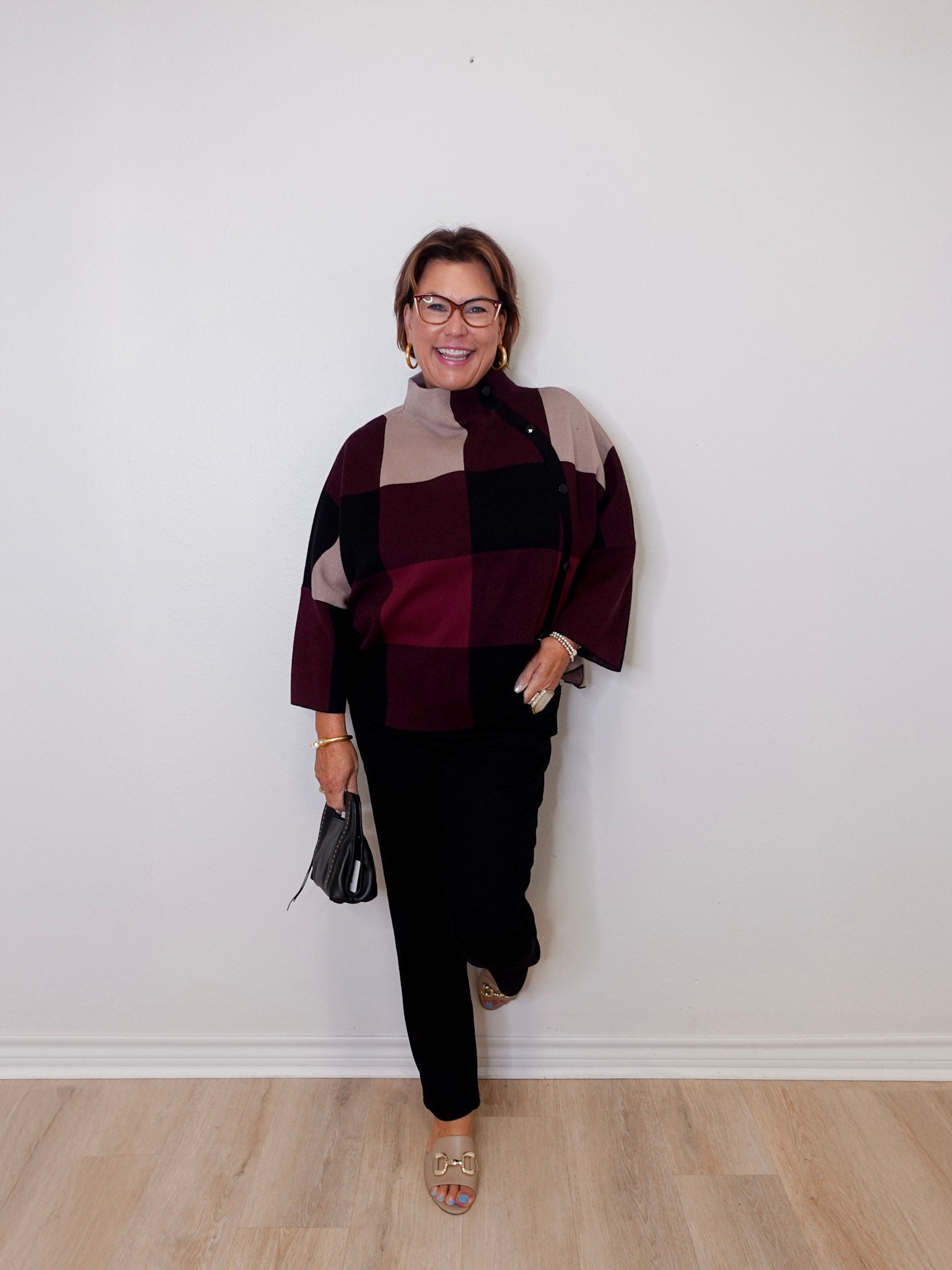 Person wearing a patterned sweater and black pants against a white wall.