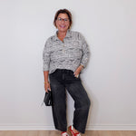 Person wearing a patterned shirt, dark jeans, and red shoes against a white wall.